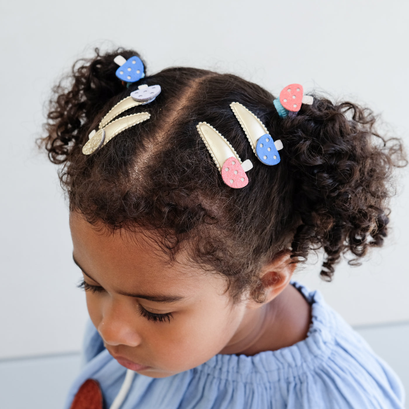Child with colourful girls hair clips and hair ponies in their hair against a light background