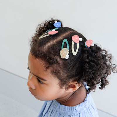 Child with colourful girls hair clips in their hair against a light background