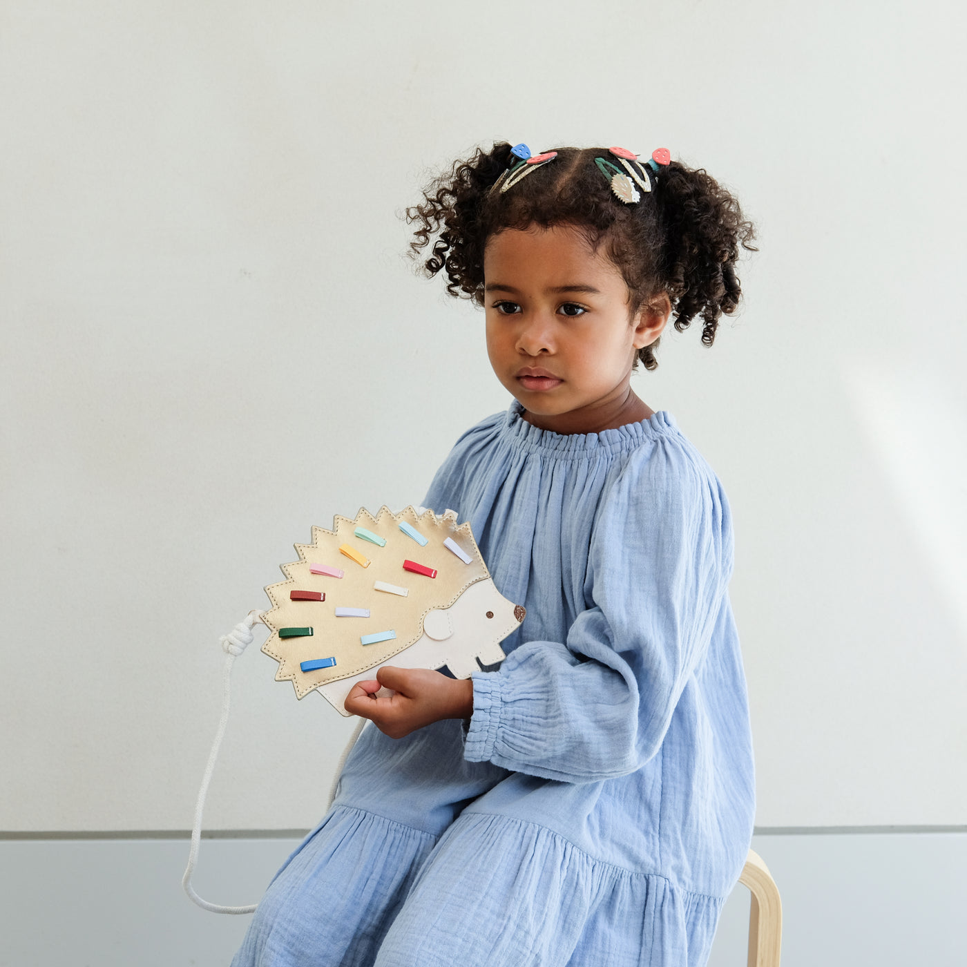 Child holding a hedgehog shaped bag with colourful spikes against a plain background