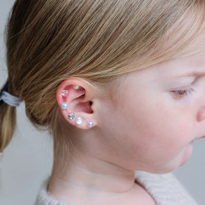 Close-up of a child's ear with multiple earrings against a neutral background