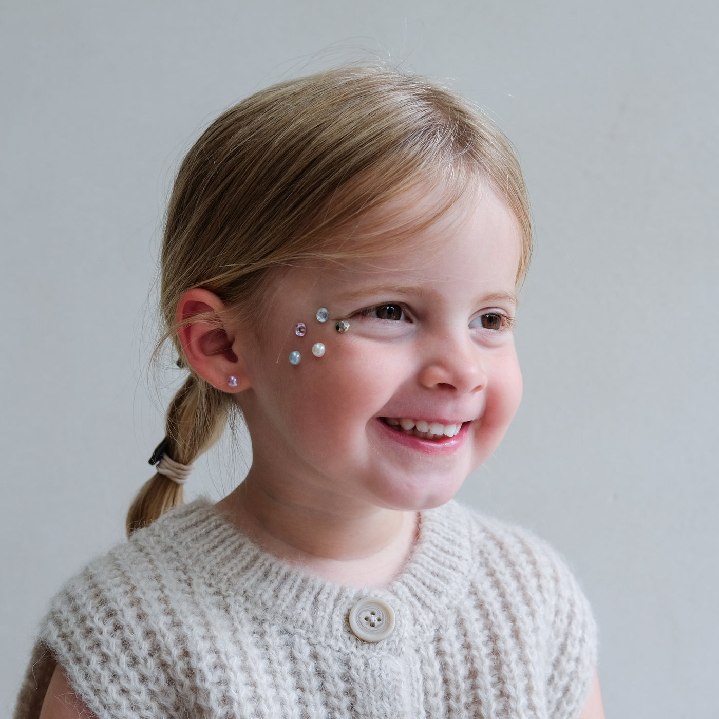 Young girl with decorative earrings smiling against a plain background