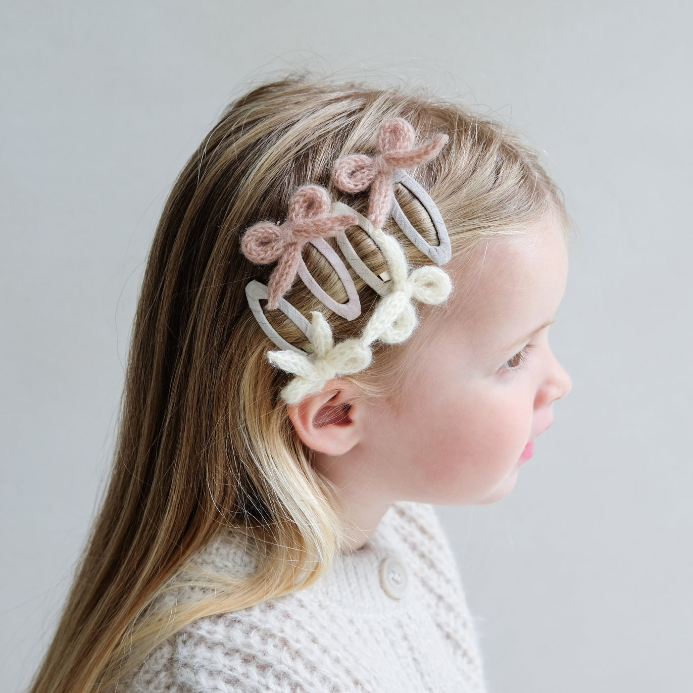 young girl wearing granny knitted bow clic clac hair clips in her hair against a white background
