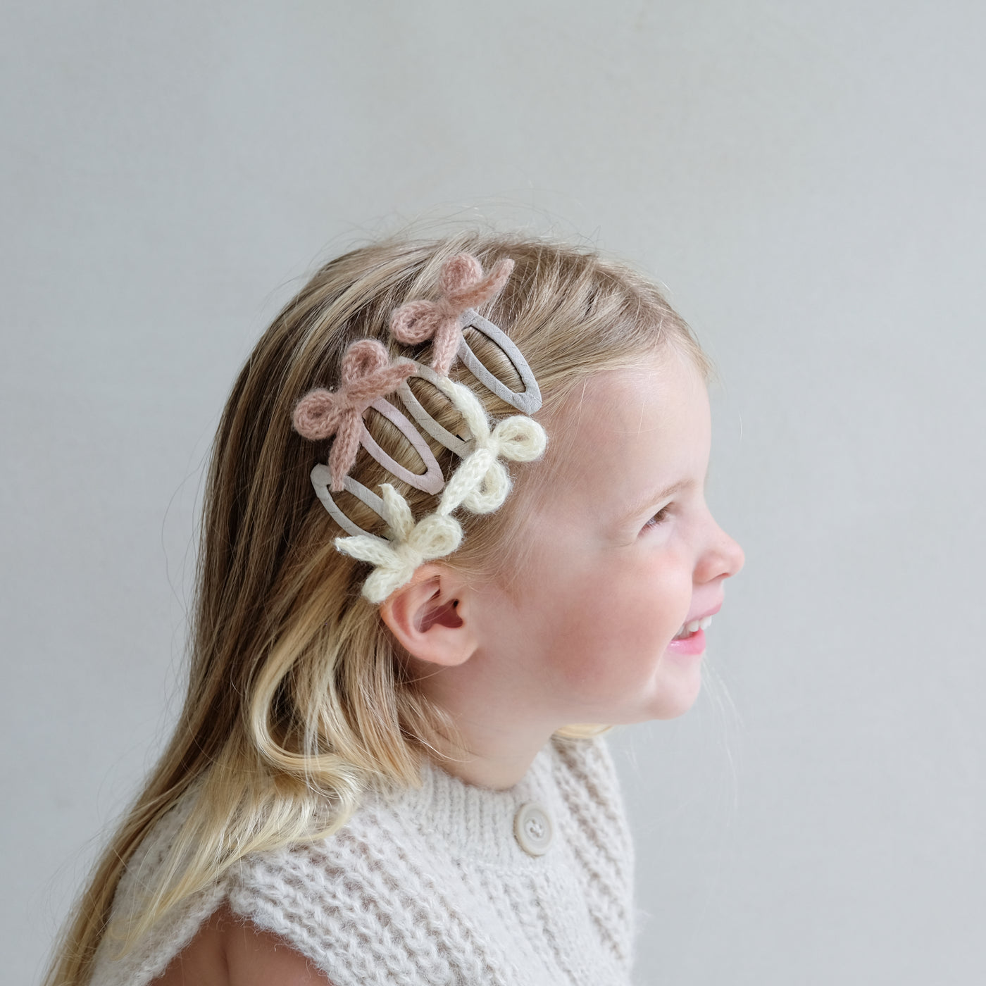 young girl wearing granny knitted bow clic clac hair clips in her hair against a white background
