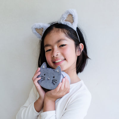 Child wearing cat ears and holding a cat-shaped jewellery box against a plain background