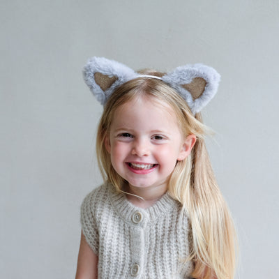 Child wearing fluffy cat ears headband with a plain background