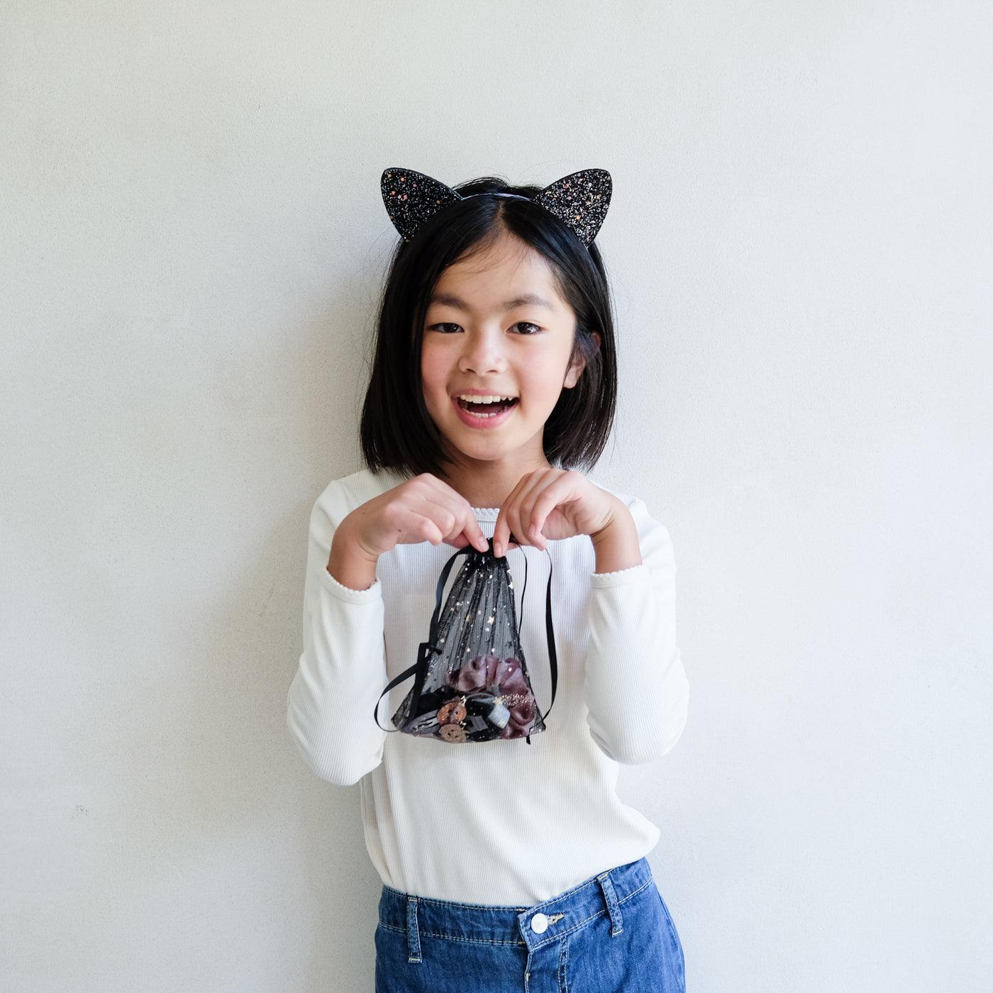 Child wearing black cat ears holding a halloween gift pouch with a white background