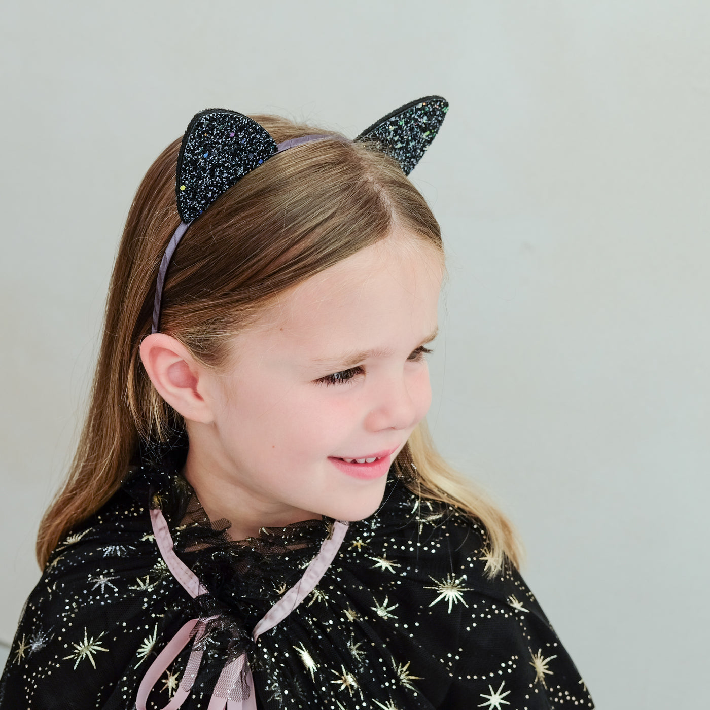 child wearing black glitter cat ears headband against a white background