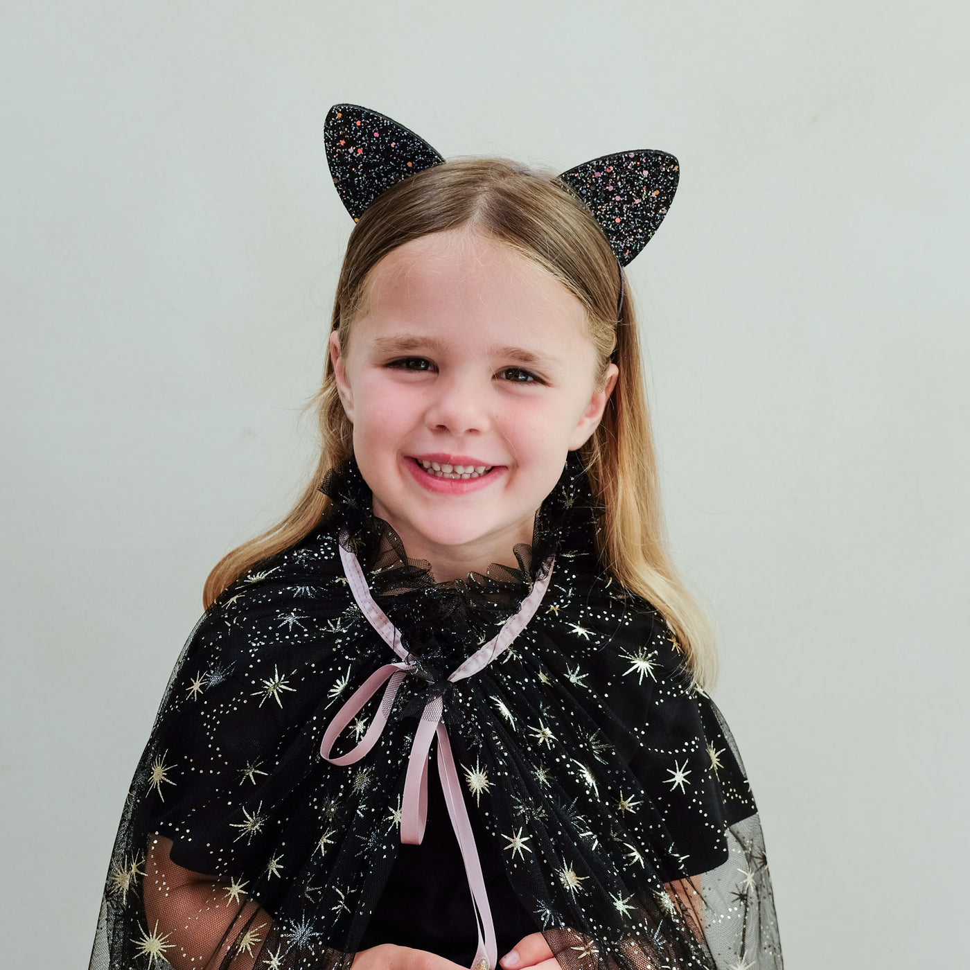child wearing glitter cat ears headband against a white background
