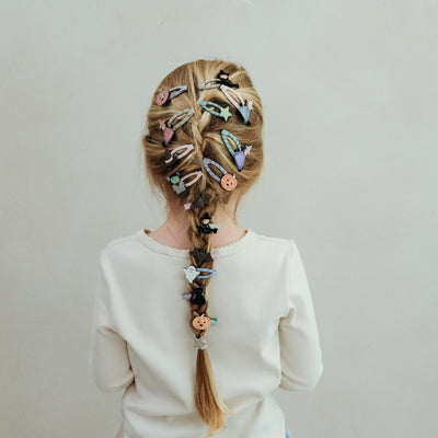 girl with hair in a braid decorated with halloween themed hair clips against a white background