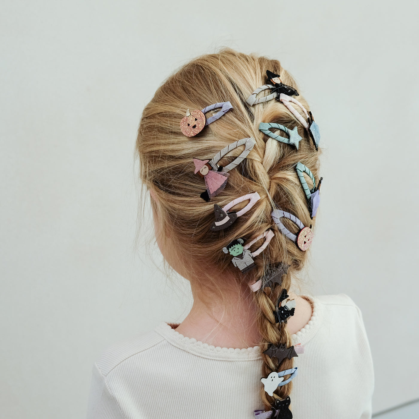 girl with hair in a braid decorated with halloween themed hair clips against a white background