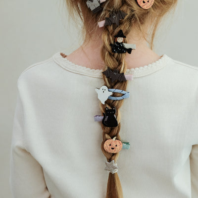 girl with hair in a braid decorated with halloween themed hair clips against a white background