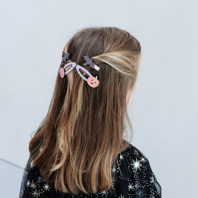 girl wearing pumpkin and bat hair clips in her hair against a white background