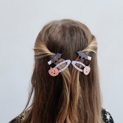 girl wearing pumpkin and bat hair clips in her hair against a white background