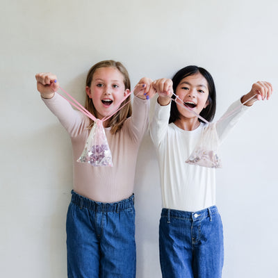 two girls holding hair accessory gift bags against a white background