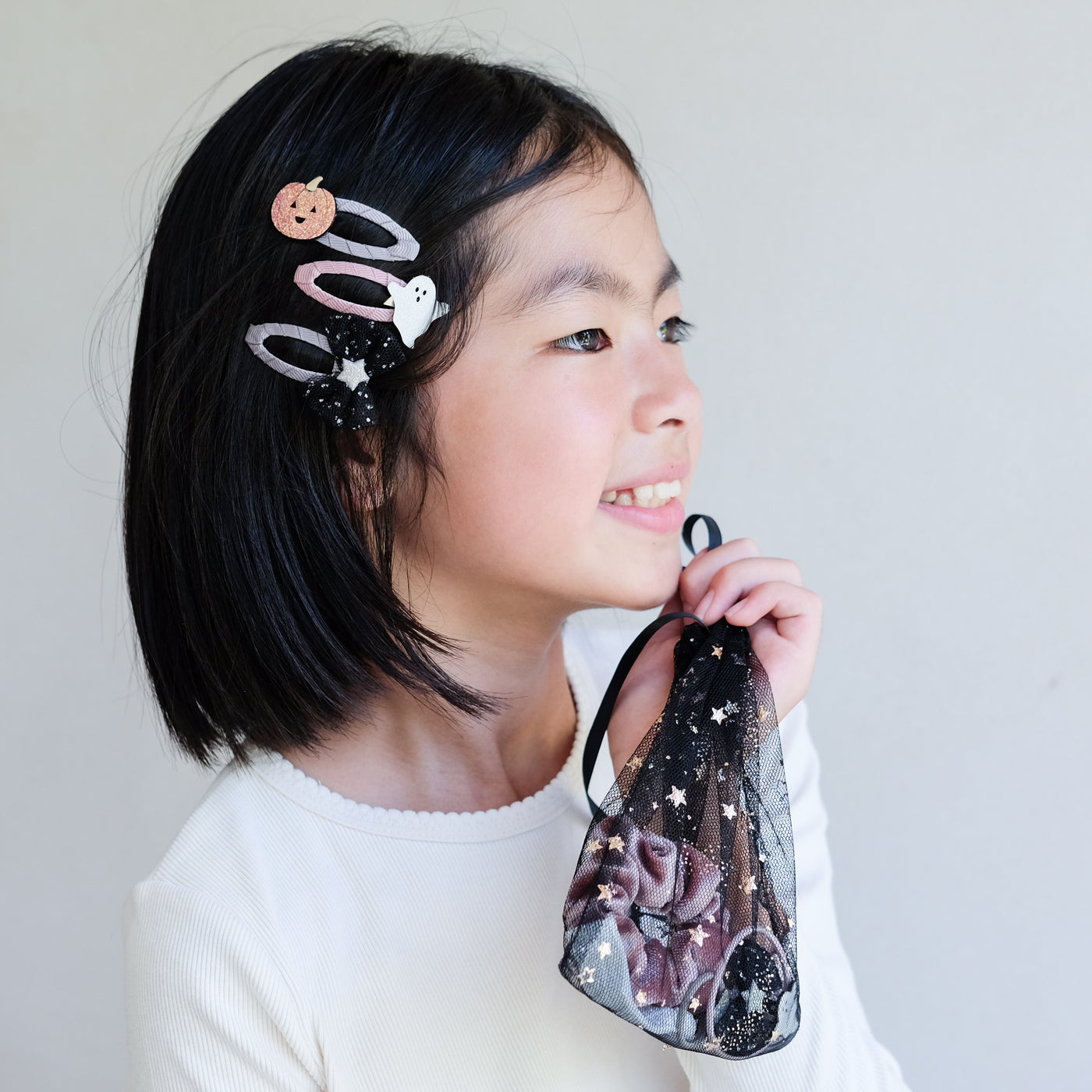 Child wearing black cat ears holding a halloween hair accessory gift bag with a white background