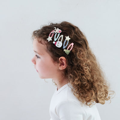 girl with curly hair wearing santa & rudolph mini clic clac hair clips in her hair against a plain background