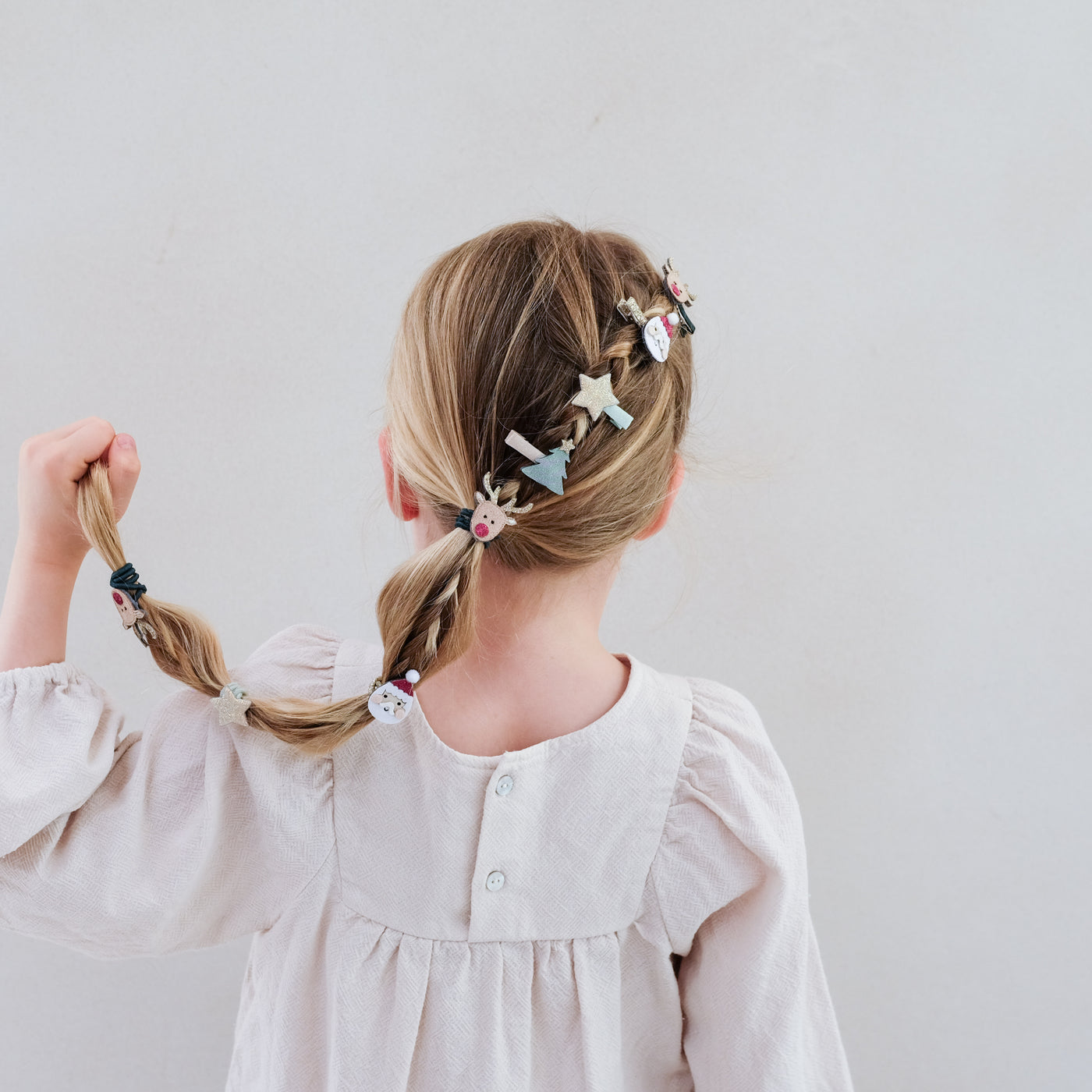 girl with hair styled in a braid wearing Santa and Christmas themed mini hair clips in her hair against a plain background