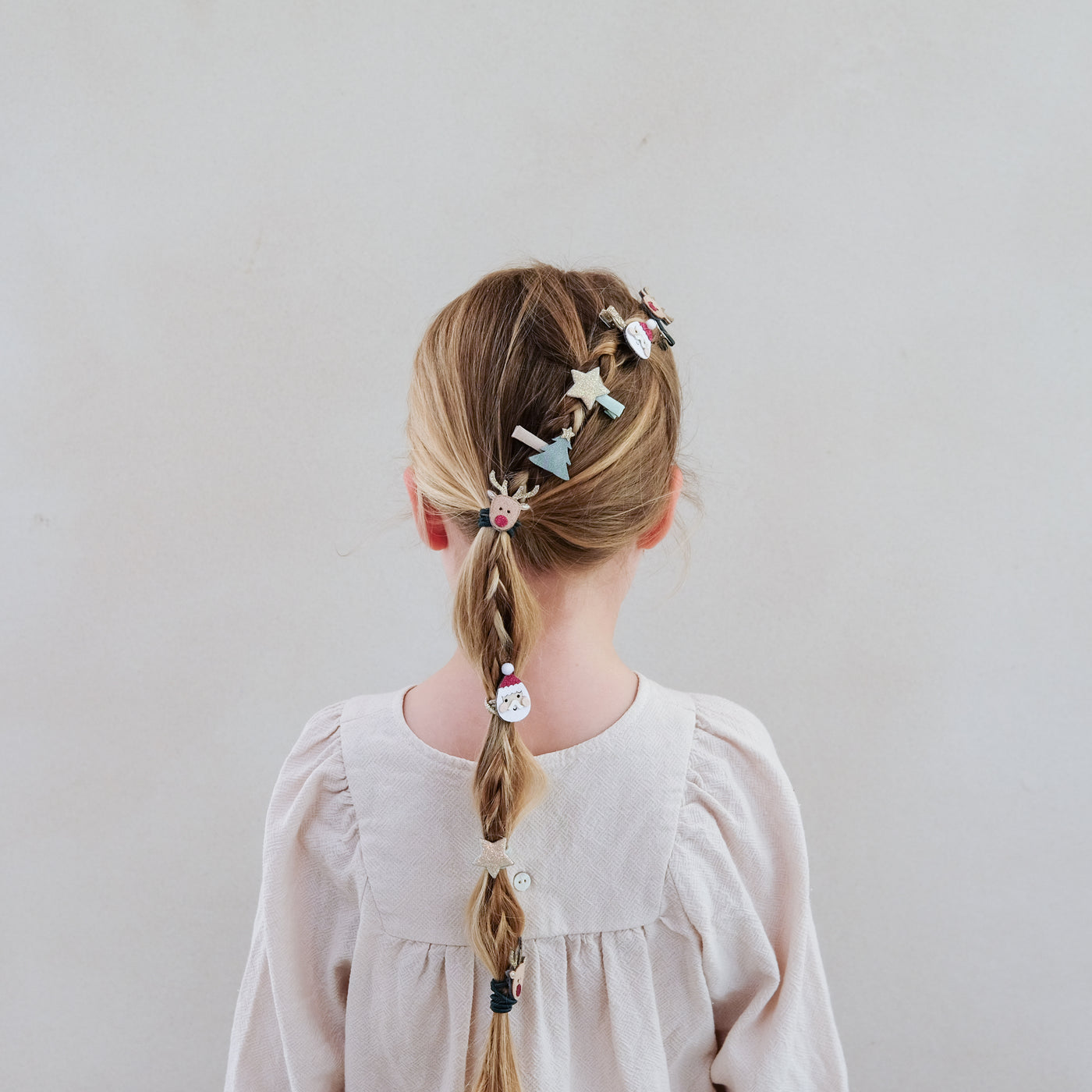 girl with hair styled in a braid wearing Santa and Christmas themed mini hair clips in her hair against a plain background
