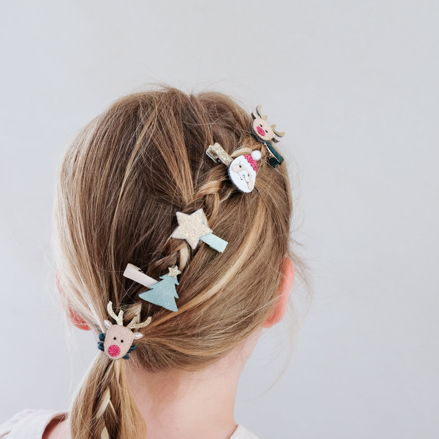 girl with hair styled in a braid wearing Santa and Christmas themed mini hair clips in her hair against a plain background