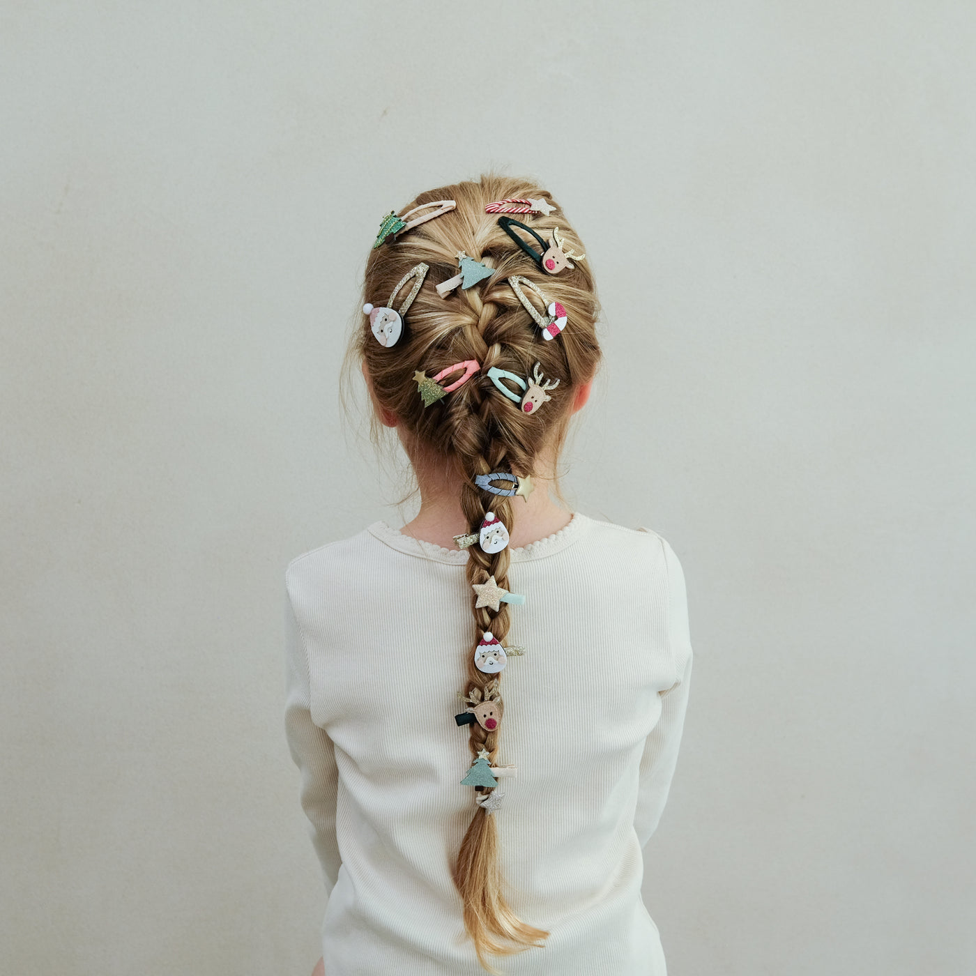 girl with hair styled in a braid wearing Santa and Christmas themed mini hair clips in her hair against a plain background
