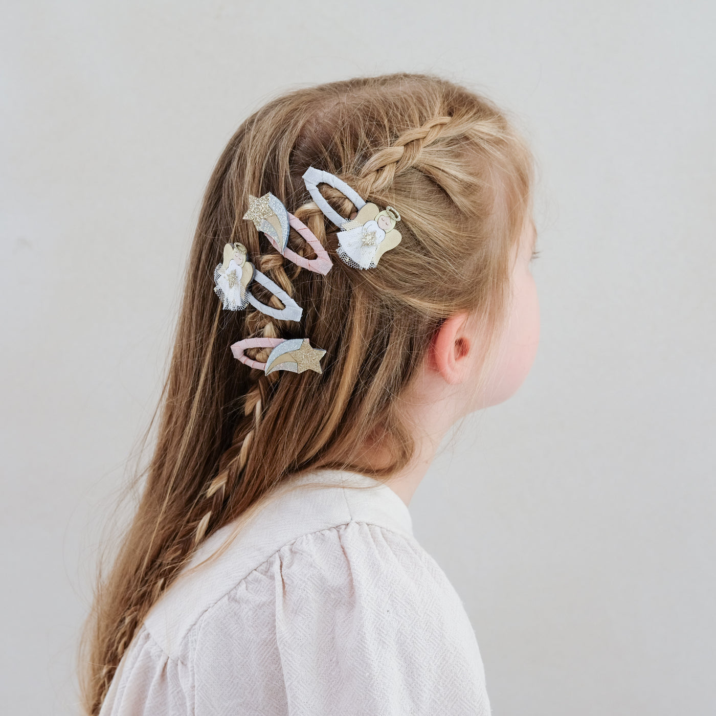 girl with braided hair wearing angel clic clacs hair clip set in her hair against a white background