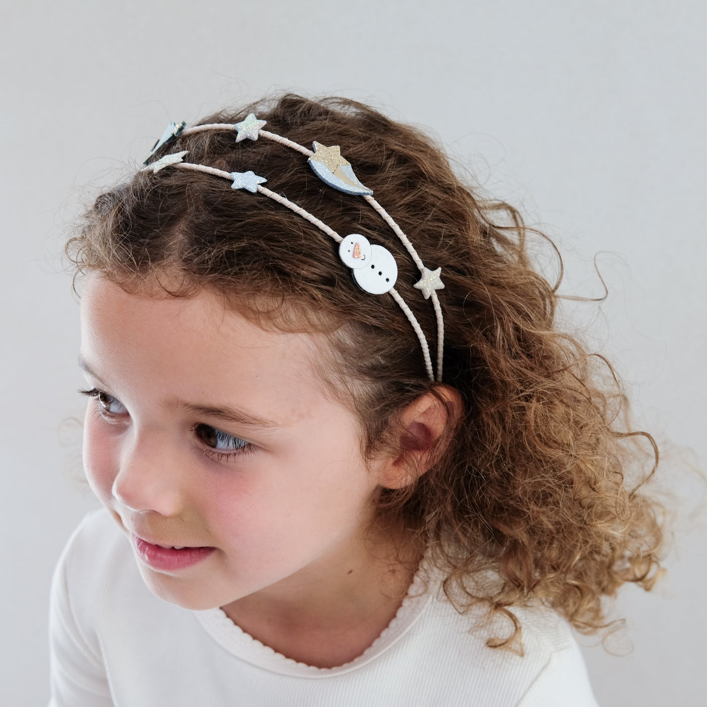 Young girl wearing a decorative headband with stars and a snowman on a plain background