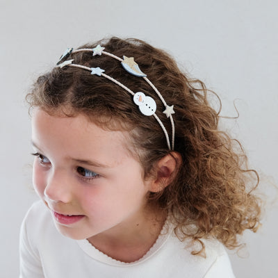 Young girl wearing a decorative headband with stars and a snowman on a plain background