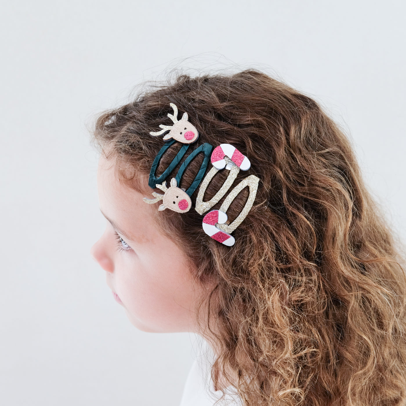 girl with curly hear wearing Rudolph & candy cane clic clacs hair clips in her hair against a white background