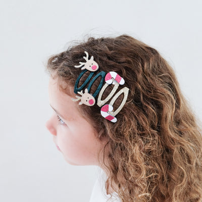 girl with curly hear wearing Rudolph & candy cane clic clacs hair clips in her hair against a white background