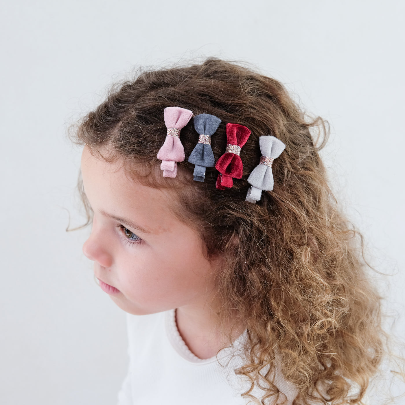 girl wearing christmas velvet bow clips in her hair against a white background
