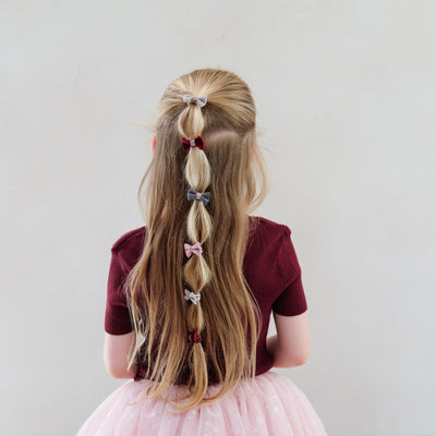 girl wearing Christmas velvet bow ponies in her hair against a white background