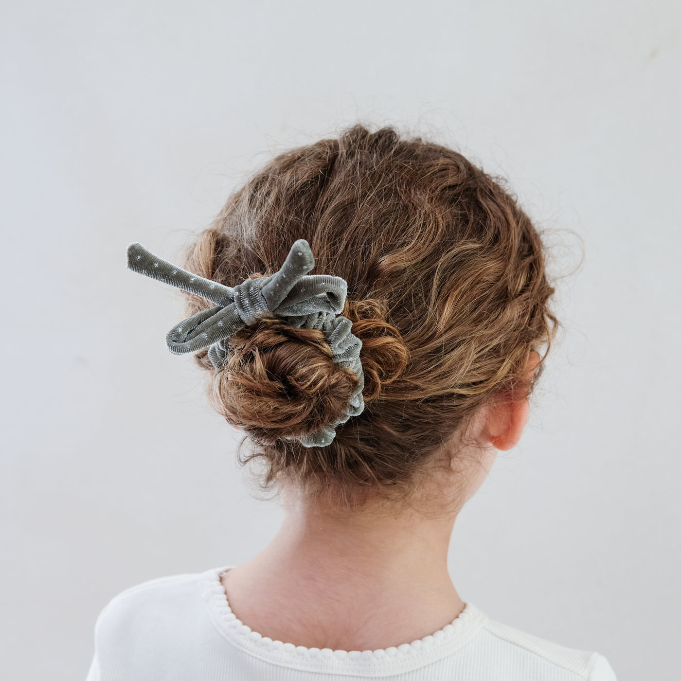 girl wearing silver velvet bow christmas scrunchie in her hair against a white background