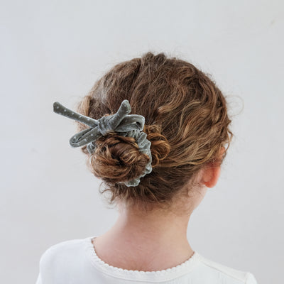 girl wearing silver velvet bow christmas scrunchie in her hair against a white background