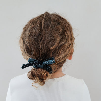 girl wearing teal velvet bow christmas scrunchie in her hair against a white background