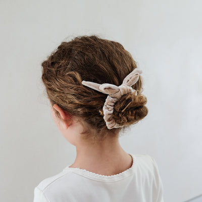 girl wearing beige velvet bow christmas scrunchie in her hair against a white background