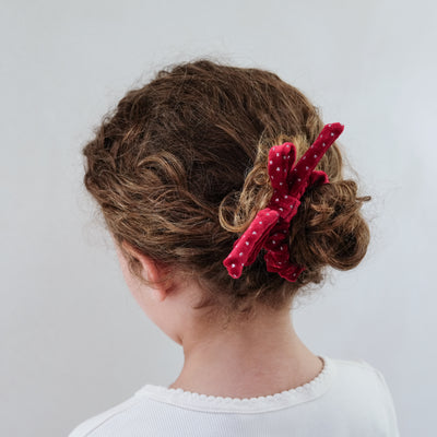 girl wearing red velvet bow christmas scrunchie in her hair against a white background
