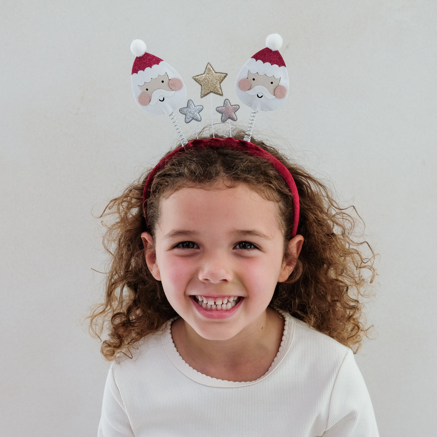 Child wearing a festive bopper headband with Santa faces and stars on a plain background