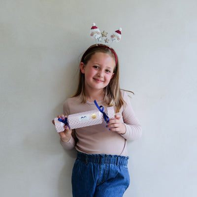 Young girl wearing festive headband holding a Christmas cracker hair accessory gift box against a plain background