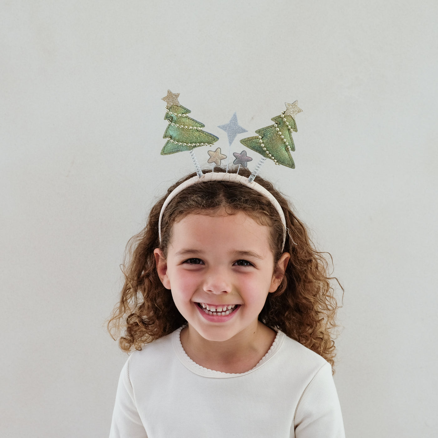 young girl wearing a Christmas tree bopper headband against a white background