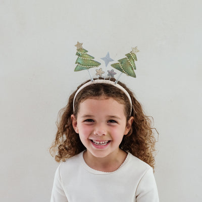 young girl wearing a Christmas tree bopper headband against a white background