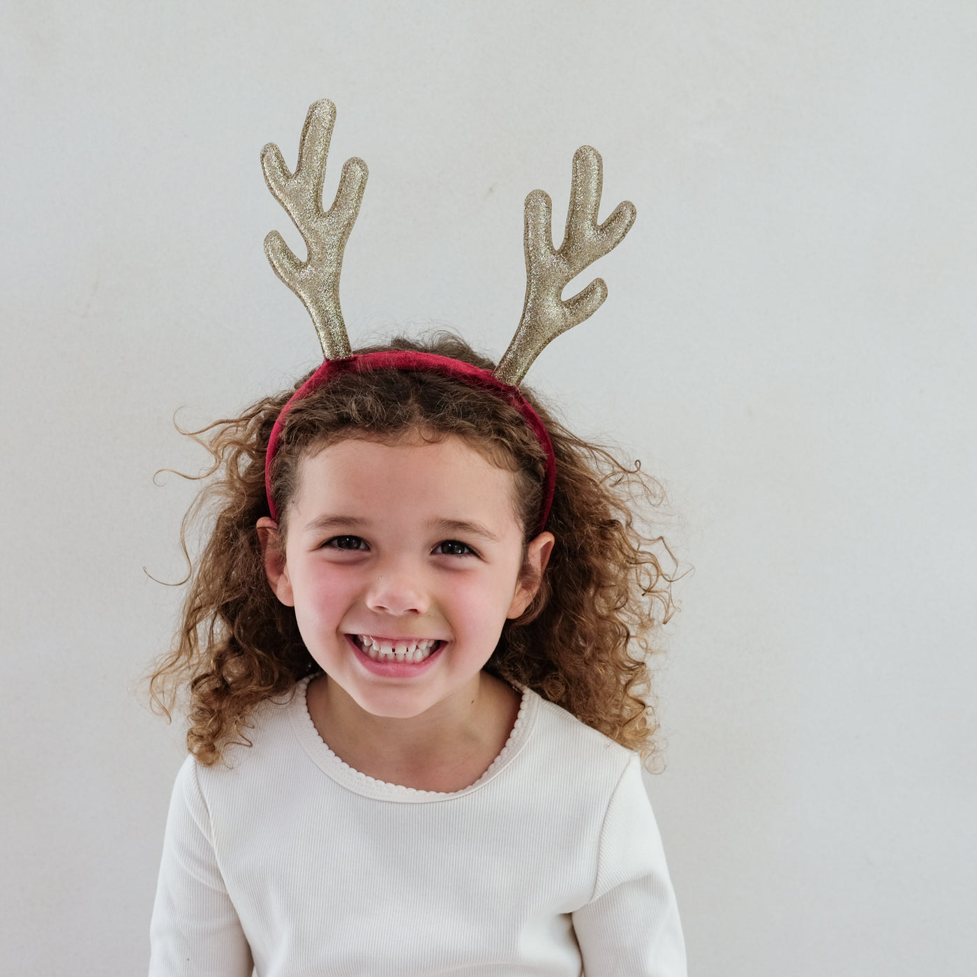 Child wearing a headband with gold antlers against a plain background