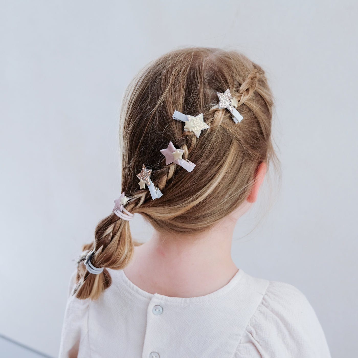 Child with braided hair wearing sparkle star mini hair clips against a plain background