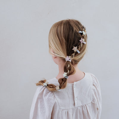 Child with braided hair wearing sparkle star mini hair clips against a plain background