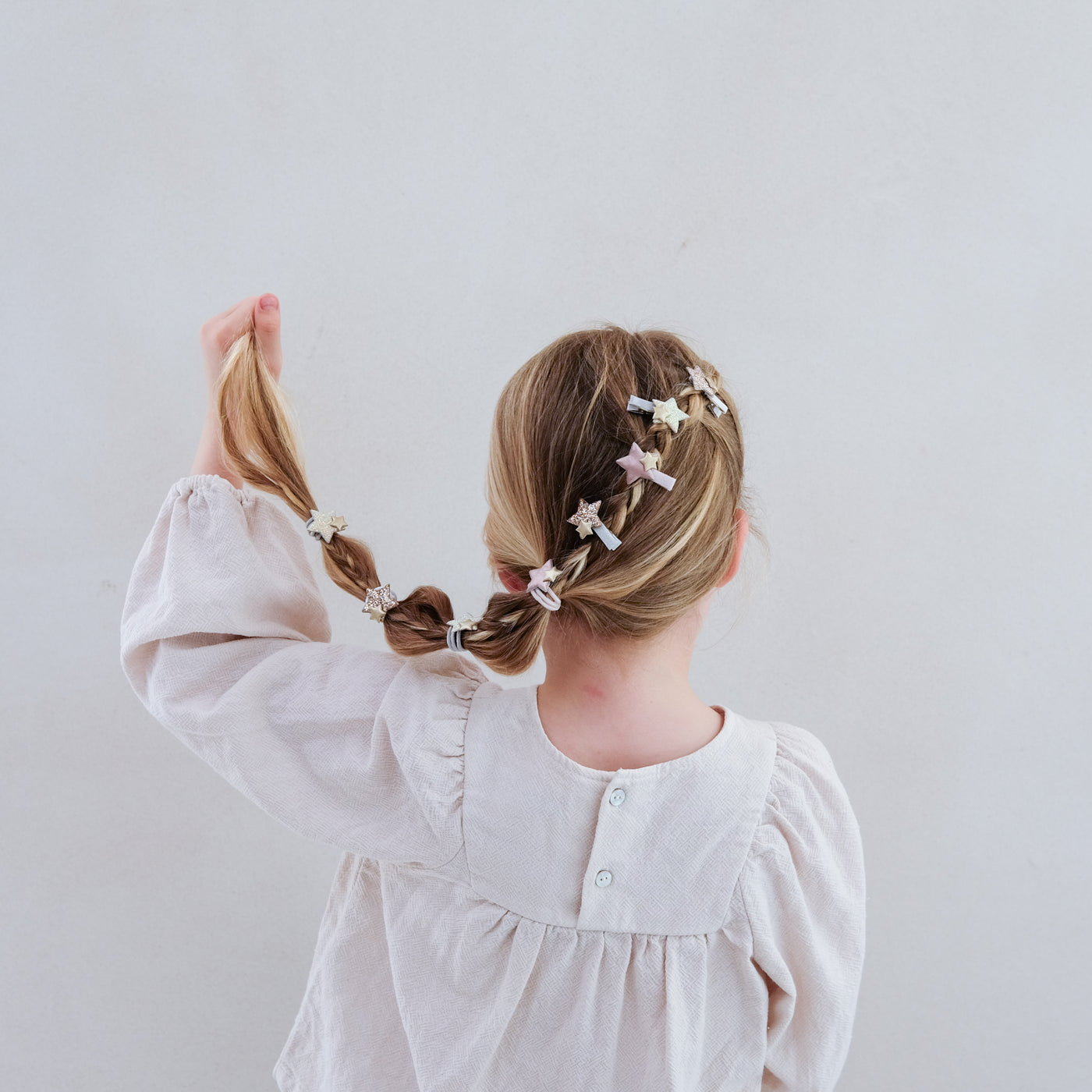 Child with braided hair wearing sparkle star mini hair clips against a plain background