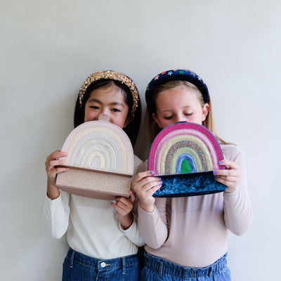 Two children holding rainbow-shaped jewellery boxes against a plain background