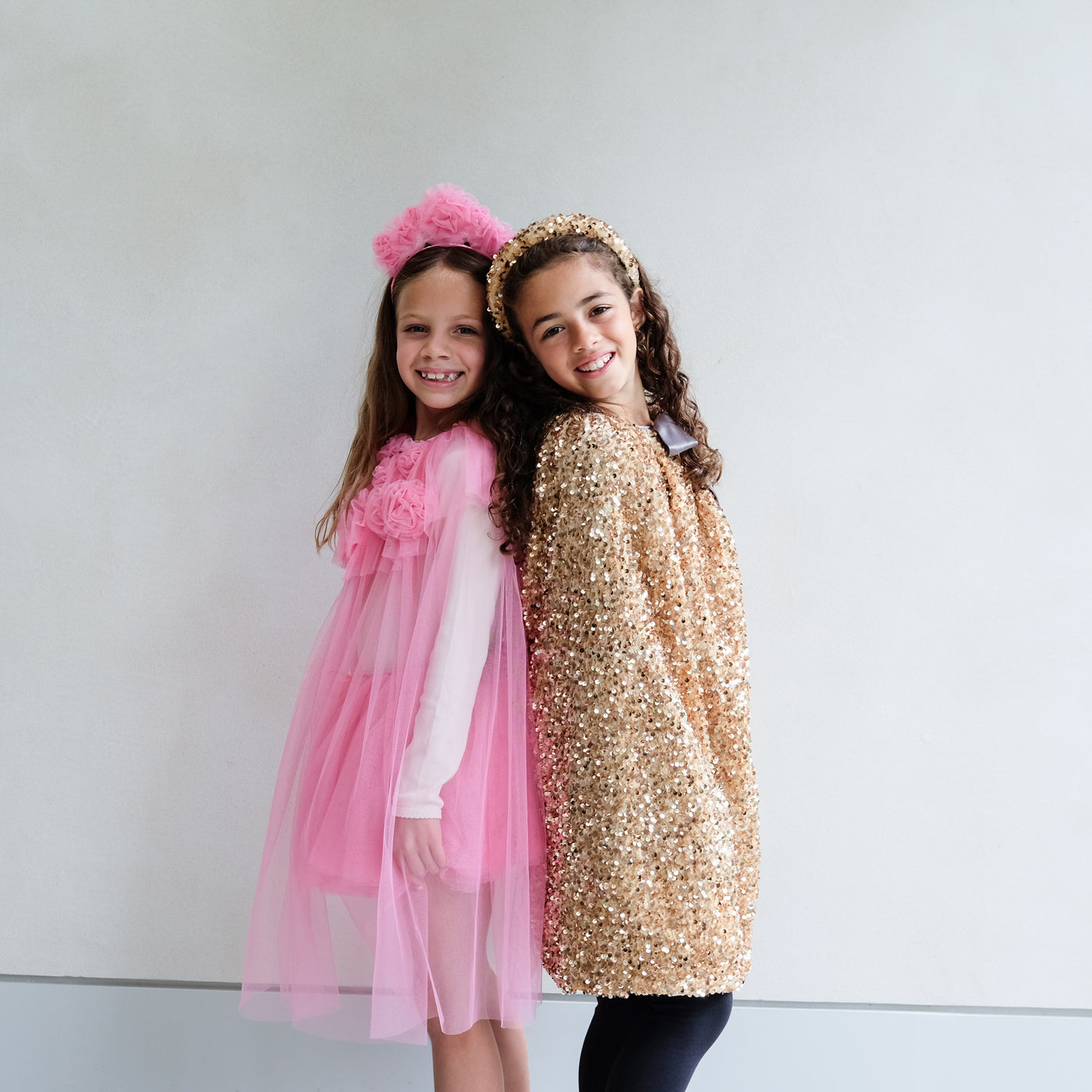 Two children in pink and gold dress up outfits with headbands against a plain background