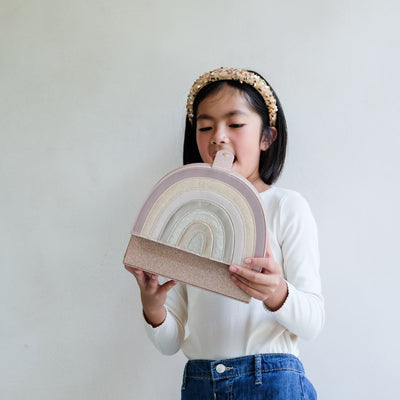 Child holding a pink rainbow-shaped jewellery box against a plain background