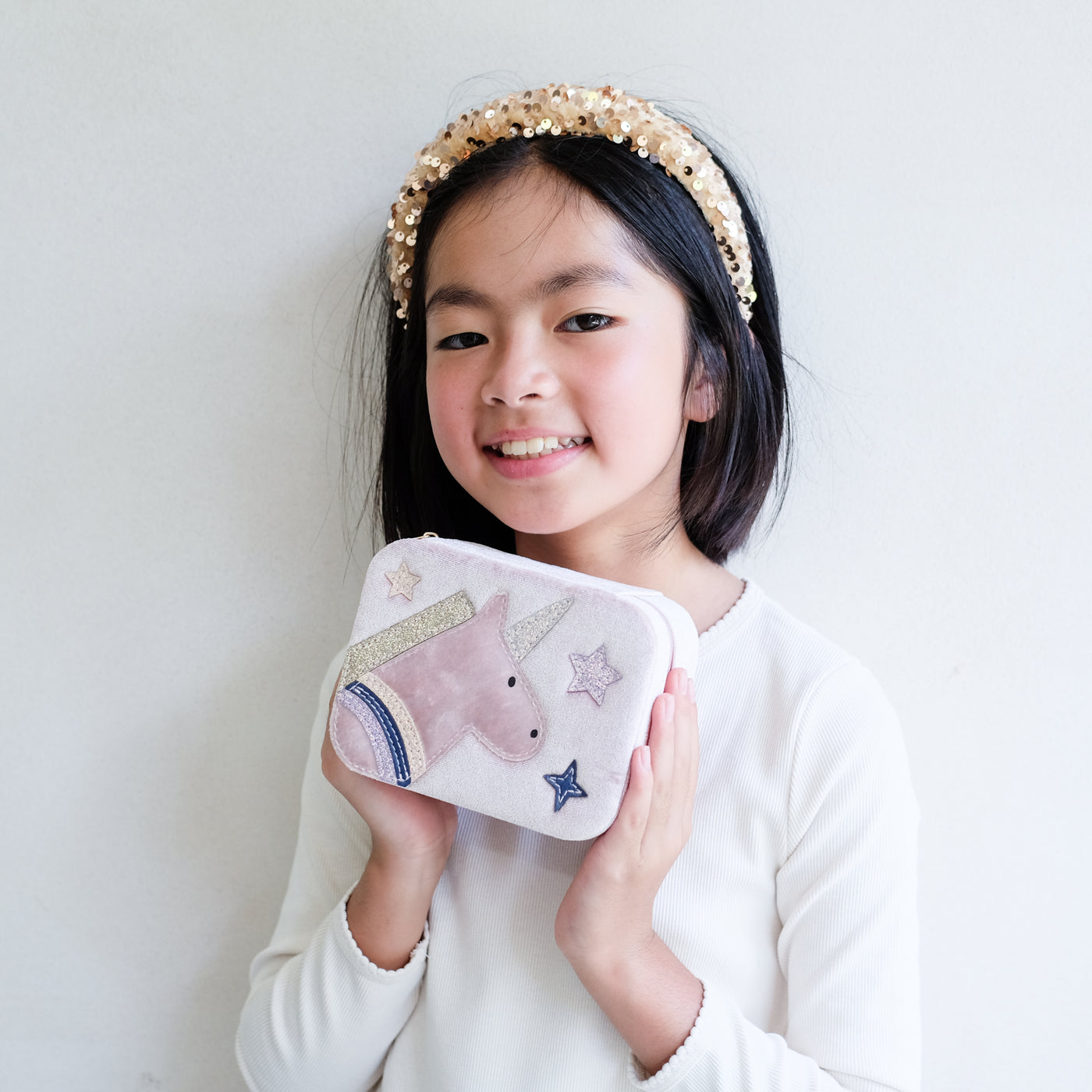 Young girl holding a jewellery box with a unicorn design against a plain background