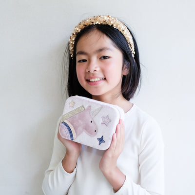 Young girl holding a jewellery box with a unicorn design against a plain background