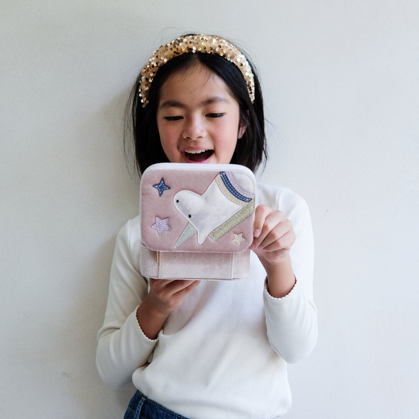 Child holding a pink jewellery box with a unicorn design against a plain background
